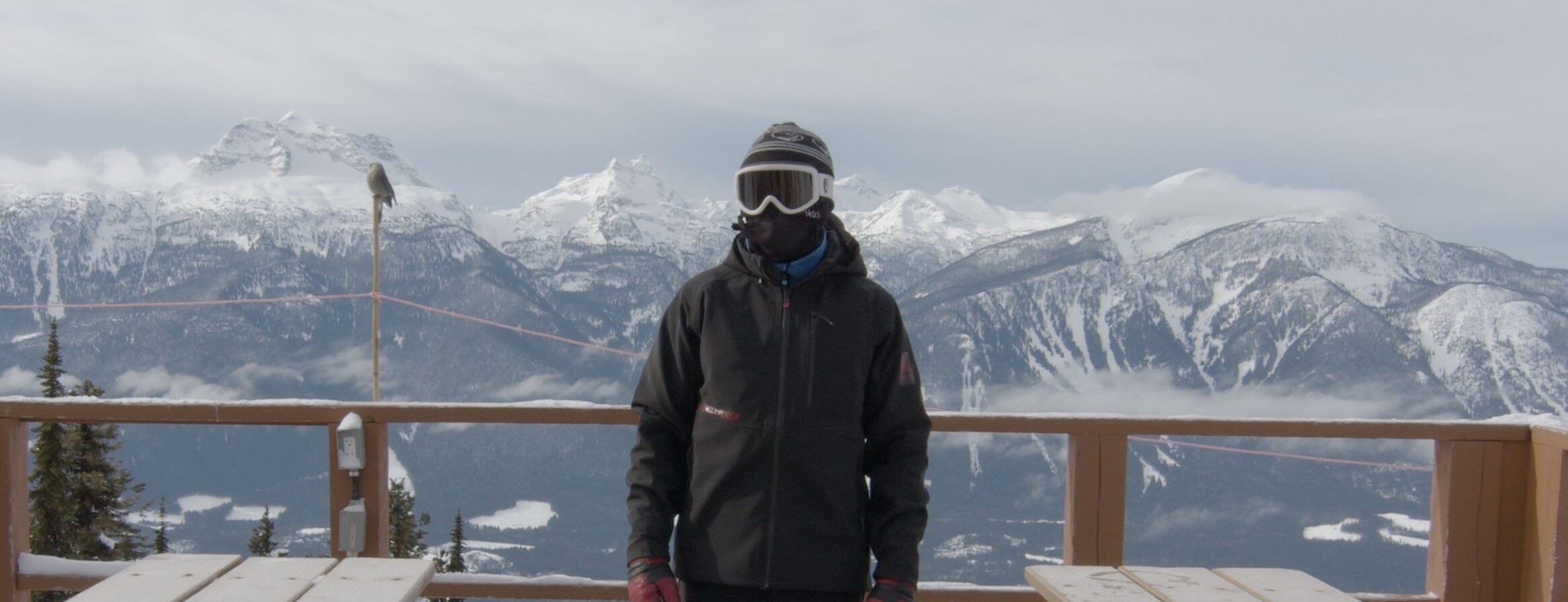 man with snow gear on looking into distance with snowy mountains behind him