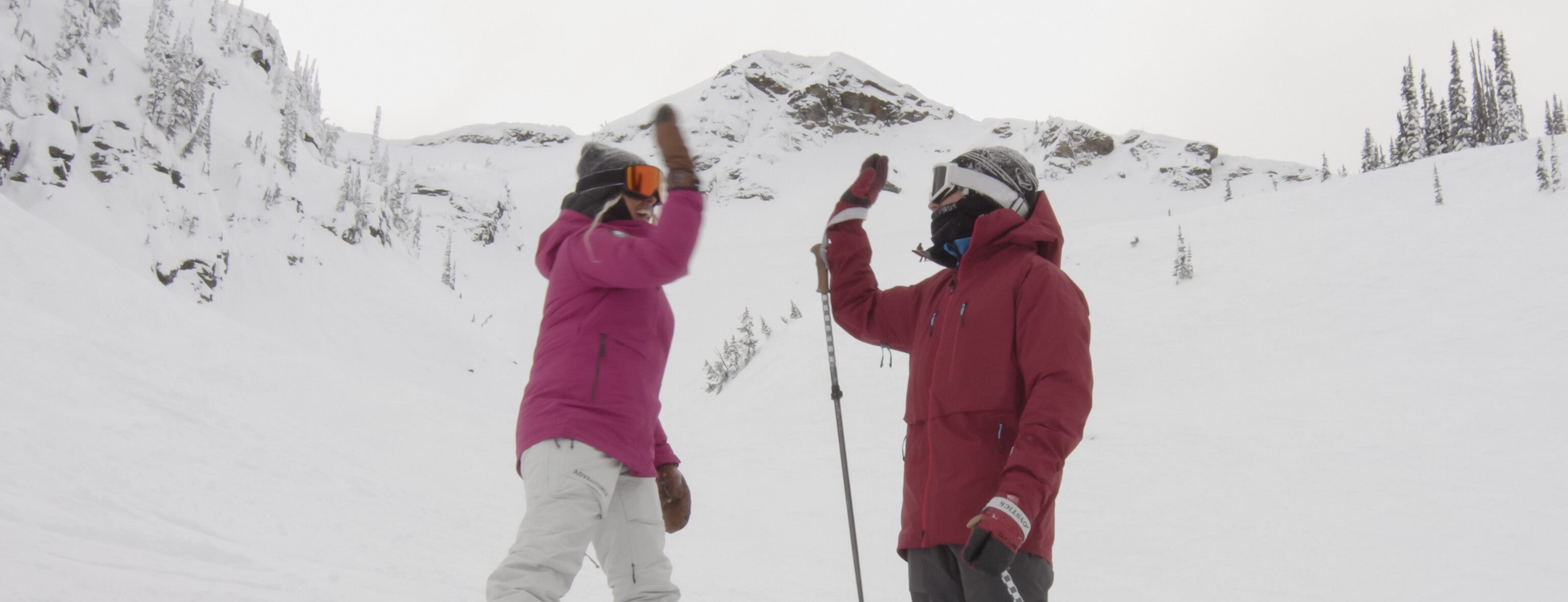 two people high fiving on snowy mountain wearing winter gear